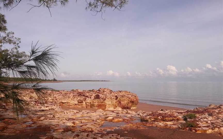 View over the ocean with sand, rocks, and part of a casuarina tree in the foreground