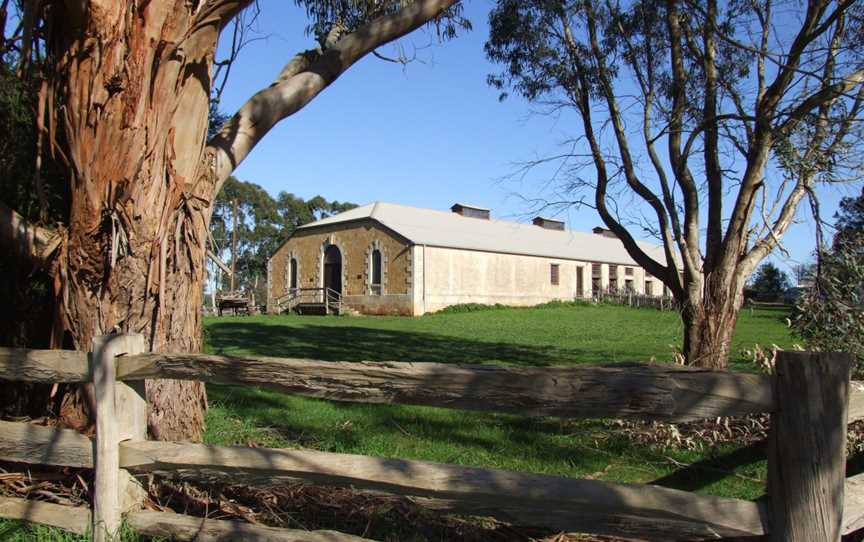 A colour photo of a historic-looking, limestone building appearing through trees in the foreground